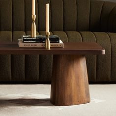 a coffee table with books on it and candles in front of a couch that's up against the wall