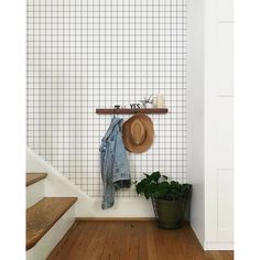 a hat and jacket hanging on the wall next to some stairs in a room with white tiled walls