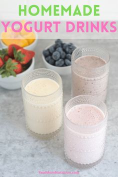 three glasses filled with yogurt next to bowls of berries and strawberries on a table