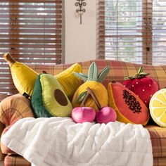 a pile of fruit sitting on top of a couch next to a window with blinds