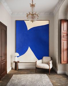 a room with a large blue painting on the wall and a white chair in front of it