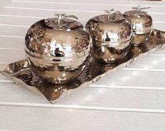 three shiny silver apples sitting on top of a metal tray next to each other in front of a white table