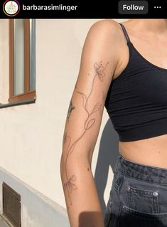 a woman with a tattoo on her arm standing in front of a white wall and window