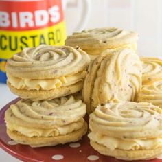 several cookies with frosting on a red plate next to a coffee cup and mug