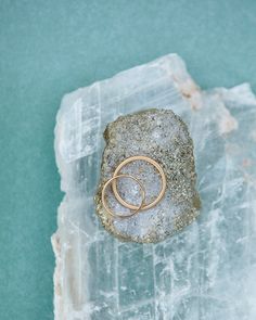 two gold rings sitting on top of a rock next to a blue water background with ice