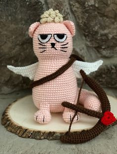 a pink crocheted cat sitting on top of a tree stump holding a bow and arrow