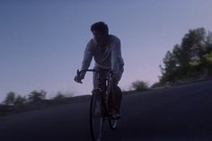 a man riding a bike down the middle of a road with trees in the background