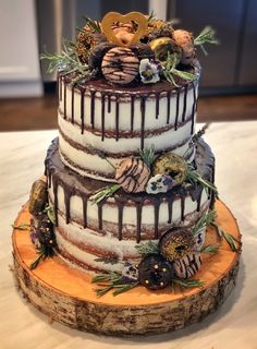 a three tiered cake with frosting and flowers on top is sitting on a wood slice