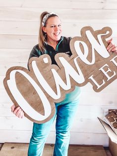 a woman holding up a wooden sign that says olive leaf on the side of her face