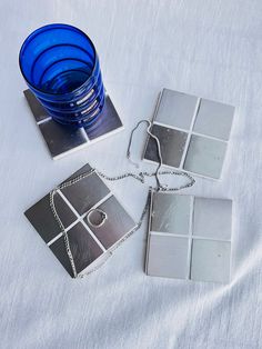 a blue glass sitting on top of a table next to two silver squares and a chain