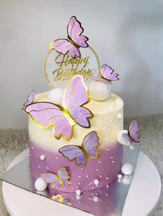 a purple and white cake with butterflies on it's top is sitting on a plate