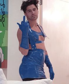 a man in blue latex is making the peace sign with his hand while standing on a bed