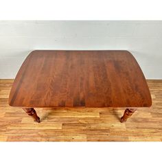 a wooden table with two leaves on the legs and a square shaped top, sitting on a hard wood floor