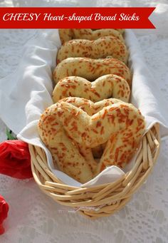 some heart shaped breads in a basket on a white tablecloth with red roses