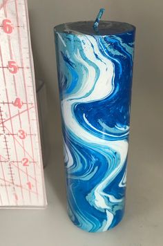 a blue and white marbled candle next to a measuring tape on a table top