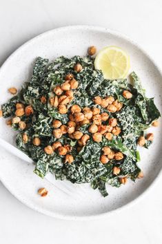 a white plate topped with spinach and chickpeas next to a lemon wedge