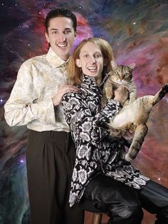 a man and woman holding a cat in front of a space background