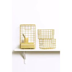 three wire baskets sitting on top of a white shelf next to a book and pen