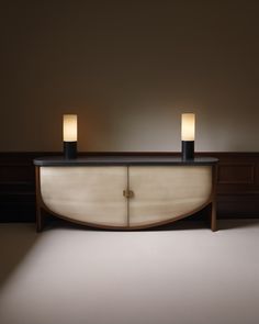 two candles sitting on top of a cabinet in the middle of a room with white walls