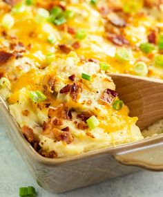 a casserole with bacon, cheese and green onions in a baking dish on a wooden spoon