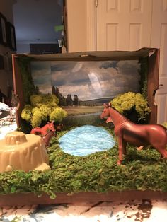 an open box filled with fake horses on top of a table next to a painting