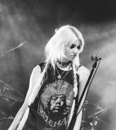 a woman with long blonde hair holding a microphone and standing in front of a stage