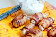 bacon wrapped sausages on a yellow plate next to a small bowl of ranch dressing