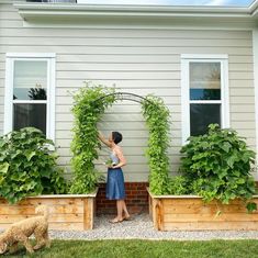 a woman standing in front of a house next to two planters filled with plants