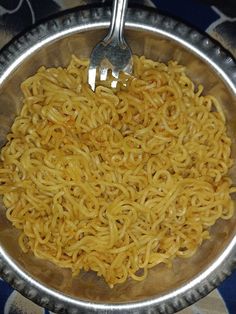 a metal bowl filled with noodles on top of a blue and white patterned table cloth