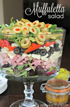 a salad in a glass bowl with olives, tomatoes and other vegetables on top