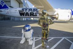 a star wars robot standing next to a space shuttle in front of an airplane on the tarmac