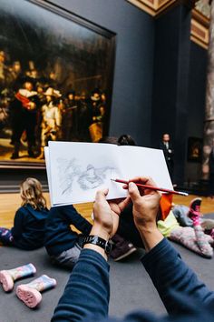 a person holding up a piece of paper in front of a painting