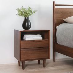 a bed with a wooden headboard and night stand next to a vase filled with flowers