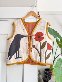 an embroidered vest hanging on a white door with flowers and a bird in the center