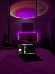 a laptop computer sitting on top of a bed in a room with purple lighting above it