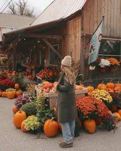 a woman standing in front of a store filled with pumpkins and other produce on display