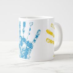 a white coffee mug with blue, yellow and orange hand prints on the outside of it