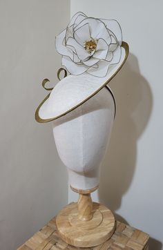 classic white, handmade saucer fascinator. Embellished with a wire, netted, white and gold rose. Sinamay base, white and trimmed with a gold brim. Gold swirl decoration.  Secured to the head with a white satin hairband and hidden mini comb. Sinamay is a natural fibre derived from the banana plant. Elegant White Round Crown Headpiece, Adjustable White Curved Brim Headpiece, White Adjustable Costume Hat With Pinched Crown, White Formal Headpiece With Handmade Flowers, White Adjustable Headpiece With Structured Crown, Formal White Handmade Flower Headpiece, White Adjustable Structured Crown Headpiece, White Party Hat With Round Crown, White Costume Hat With Round Crown For Parties