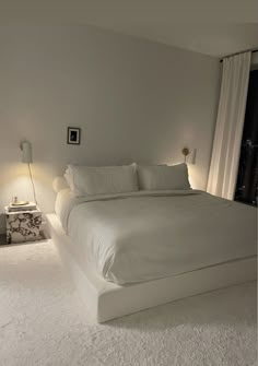 a white bed sitting in the middle of a bedroom next to a window with curtains