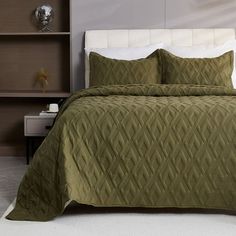 a bed with green bedspread and pillows in a room next to a bookcase