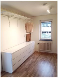 an empty room with wooden floors and white cabinets in the corner, next to a window