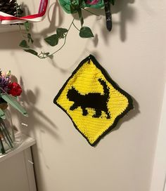 a crocheted dog crossing sign hanging on the wall next to flowers and scissors