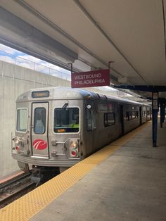 a silver train pulling into a station next to a loading platform with a sign on it