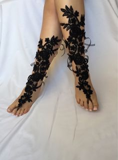 a woman's feet with black lace and flowers on the toes, sitting on a white sheet