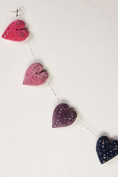 three hearts hanging from a string on a white surface with tiny dots and beads attached to the strings