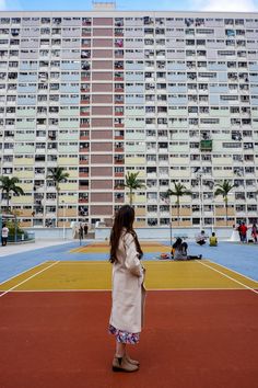 a woman standing on top of a tennis court next to a tall building with balconies