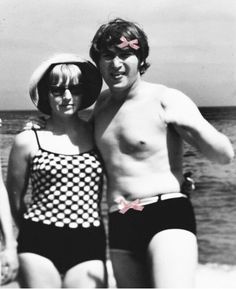 two people standing next to each other on the beach in bathing suits and sun hats