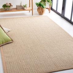 a beige rug with green pillows on the floor next to a wooden shelf and potted plant