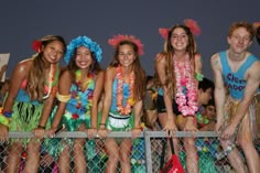 a group of young people standing next to each other near a fence with hula skirts on