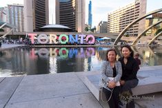 two women sitting next to each other in front of a lake with the word toronto painted on it